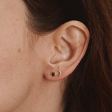 Woman wearing a gold crescent moon stud earring paired with a small gold star stud.