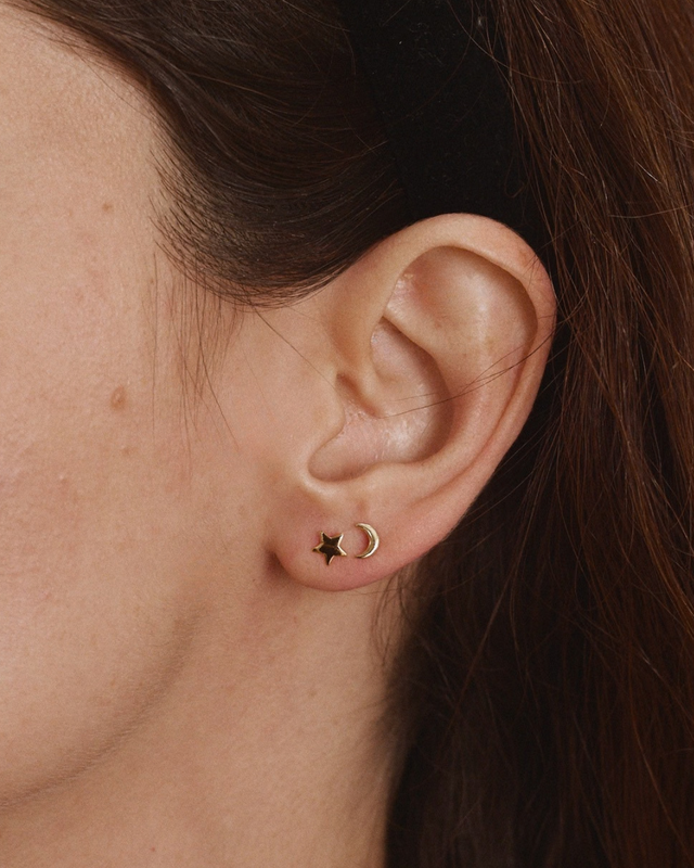 Woman wearing a gold crescent moon stud earring paired with a small gold star stud.